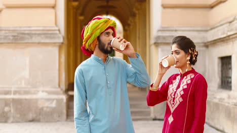 Hindu-woman-with-dot-on-forehead-and-man-in-turban-standing-outdoors,-talking-and-drinking-coffe-or-tea.-Resting.-Male-and-female-sipping-drink-and-spending-time-together.